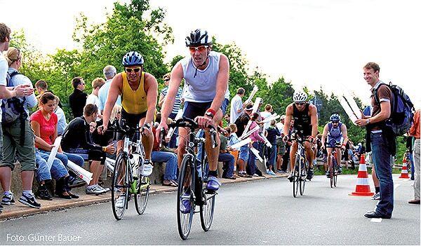 Foto: Triathleten fahren mit den Rennrad an applaudierenden Zuschauern vorbei