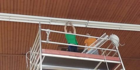 Beleuchtungs-Montage in der Haupthalle Zwei Personen montieren eine neue Beleuchtung an der Decke der Haupthalle auf einem Gerüst.