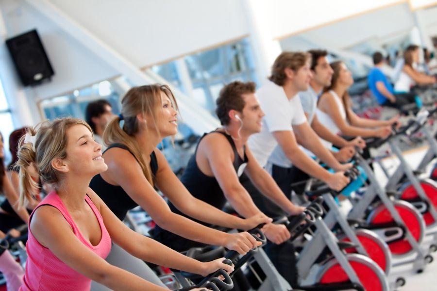 Spinning-Kurs im Fitnessstudio Mehrere Personen trainieren auf stationären Fahrrädern in einem hellen Fitnessstudio.