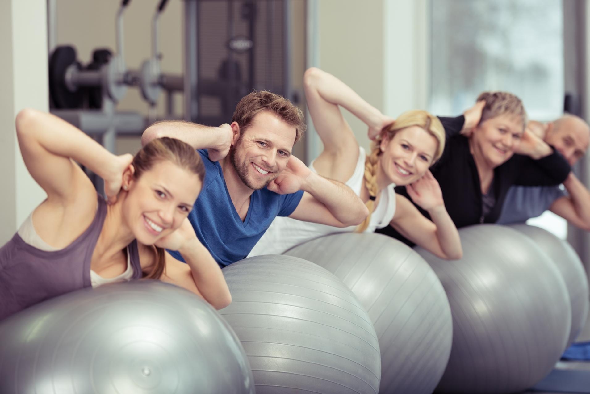 Fitnesskurs mit Gymnastikbällen Eine Gruppe von Menschen lehnt sich auf Gymnastikbälle und macht eine Übung mit den Händen hinter dem Kopf.