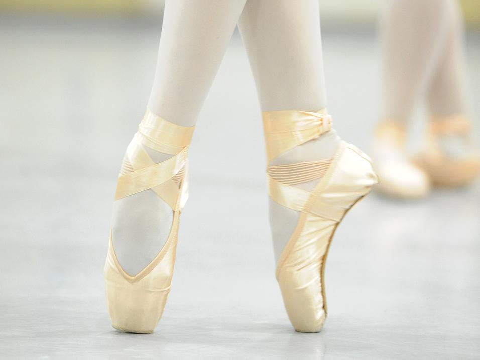 Ballettschuhe eines Tänzers auf getanzten Füßen, umgeben von unscharfen Hintergründen im Studio.